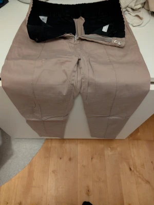 Beige chinos från Tiger of Sweden - Snygga beige chinos från Tiger of Sweden med elastisk midja och dragkedja. De har en modern passform och stilrena sömmar. Perfekta för dig som vill ha ett clean och trendigt look. Materialet är mjukt och bekvämt.