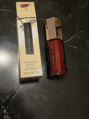 Fenty Beauty Gloss Bomb Riri 08 - Fenty Beauty Gloss Bomb Universal Lip Luminizer i färgen Riri 08. Läppglanset har en snygg röd nyans med glansig finish och kommer i en lyxig, sexkantig förpackning med roséguldfärgat lock. Innehåller 9 ml.