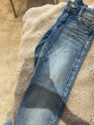 Blå jeans från Replay med broderi - Snygga blå jeans från Replay med klassisk femficksmodell och coolt broderat mönster på bakfickorna. Jeansen har en lätt tvättad look och raka ben. Perfekta för dig som gillar en avslappnad men trendig stil.