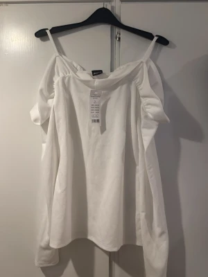 Vit frill cold shoulder topp Gina Tricot - Snygg vit cold shoulder topp från Gina Tricot med volangdetaljer och tunna axelband. Toppens material känns mjukt och har en lätt struktur, perfekt för en fräsch och stilren look. Passar dig som gillar trendiga och feminina plagg. Ny pris 299