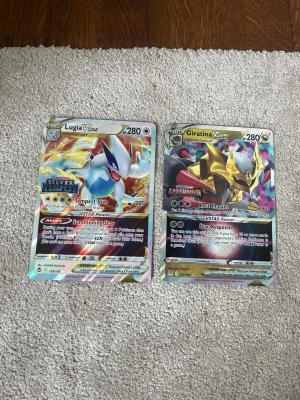 Pokémonkort Lugia VSTAR & Giratina VSTAR - Två Pokémonkort: Lugia VSTAR från Silver Tempest och Giratina VSTAR från Lost Origin. Båda korten är holografiska med färgstarka motiv och detaljerad design. Perfekt för samlare eller Pokémonfans som vill utöka sin kortsamling.