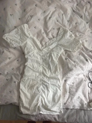 Vit klänning med v-ringning - Snygg vit kortklänning med v-ringning och korta puffärmar. Klänningen har omlottdetalj framtill och är figurnära i modellen.