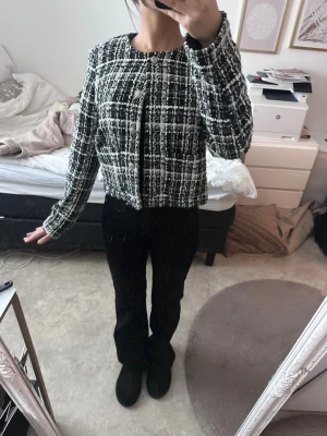 Svartvit kavaj/jacka  - Stilren svartvit kavaj i tweed med rutigt mönster och rund halsringning. Boxy och kortare passform med långa ärmar, perfekt för att lyfta en outfit. Kavajen har en klassisk look och stängs framtill. Materialet är strukturerat och ger en trendig vibe.