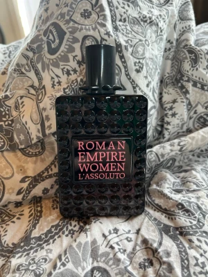 Roman Empire Women L'Assoluto parfym - Snygg parfymflaska från Roman Empire Women L'Assoluto. Flaskan är svart med en cool bubblig struktur och rosa text på framsidan. Rektangulär form och svart kork. Perfekt för dig som gillar unika och stilrena parfymer.Parfymen är full och oöppnad, säljer då jag redan har en som används. Den luktar väldigt gott   