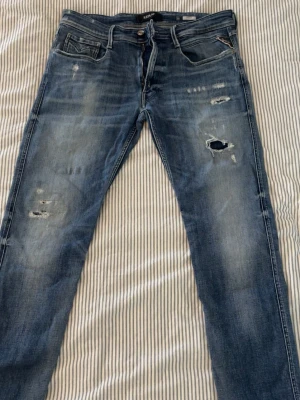 Replay anbass Jeans - Replay jeans med asfeta slitningar och riktigt feta fades🔥 Sitter sjukt bra på benen och är enkla att matcha till många olika outfits. Storlek W36 L34 och i fint skick ✨  Vid intresse är det bara att lägga ett bud eller skriva vid minsta fråga eller fundering 💪🏽