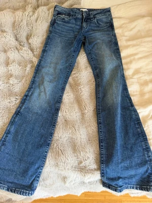 Blå bootcut jeans med broderade fickor - Snygga blå bootcut jeans med klassisk femficksdesign och broderade detaljer på bakfickorna. Jeansen har en lätt tvättad look och vida ben. Perfekta för dig som gillar 2000s stilen, använda 1 gång , super fina och bra skick🩵