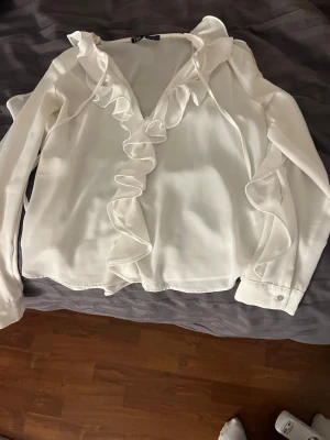 Vit volangblus från Zara - Snygg vit blus från Zara med långa ärmar och volangdetaljer längs knäppningen och axlarna. Endast använd fåtal gånger!