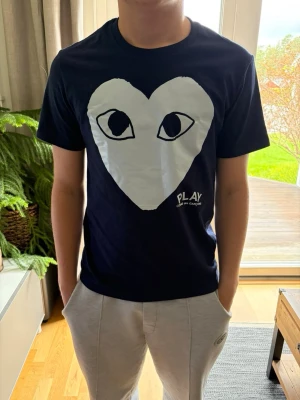 Mörkblå Comme des Garçons Play t-shirt - Mörkblå CDG T-shirt som är  i bra skick. T-shirten säljs för den är lite tight. Skriv om du har nå funderingar.