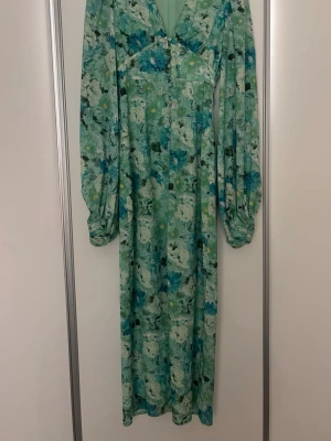 Adoore Blommig långklänning med knappar  - Långklänning i grönt och blått med blommigt mönster och v-ringning. Klänningen har långa puffärmar och knappar framtill. Från adoore i storlek 34. 