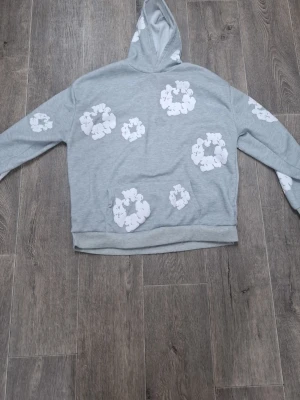 Grå hoodie med vita nalletryck - Grå hoodie med huva och vita tryck av nallar i olika storlekar över hela tröjan. Hoodien har en klassisk passform, ribbade muddar och en magficka. Perfekt för en avslappnad och trendig stil.