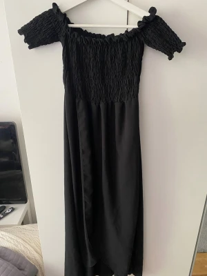Svart offshoulder långklänning - Svart långklänning med smockad överdel, slits och offshoulder-korta ärmar. Från boohoo