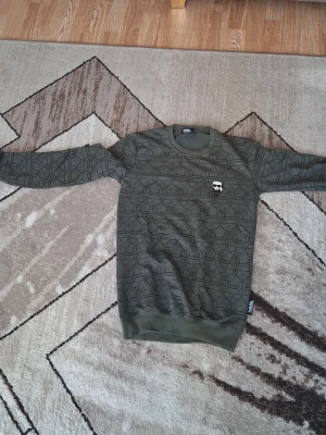 Grön Karl Lagerfeld sweatshirt - Cool grön sweatshirt från Karl Lagerfeld med heltryck av ikoniska Karl Lagerfeld-figurer. Tröjan har rund hals, långa ärmar och ribbade muddar. Perfekt för dig som gillar streetstyle och vill sticka ut med ett designerplagg.
