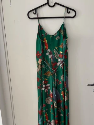     grön jumpsuit  - Grön jumpsuit i satängliknande material med blommigt mönster och justerbart midjeband. Den har en bekväm passform och kan bäras både till festliga tillfällen och under sommaren.