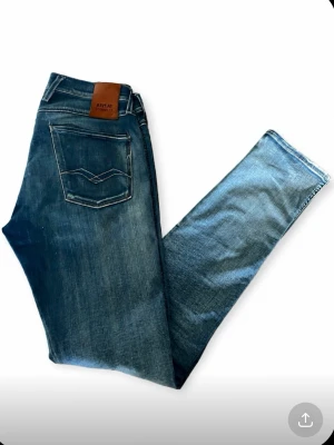 Blå jeans från Replay, modell 31/34 - Snygga blå jeans från Replay med klassisk femficksdesign och coola detaljer på bakfickan. Jeansen har en skön passform och är tillverkade i bomull med en lätt tvättad look. Perfekta för dig som gillar stilrena och tidlösa jeans.