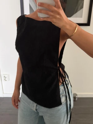 Svart ärmlös topp med snörning i sidan - Weekday strl 36 - Svart ärmlös topp med snörning i sidorna och rak halsringning. Toppen har en stilren och modern look med öppen sida och smickrande passform. Perfekt att styla med jeans eller kjol för en trendig outfit. Oanvänd