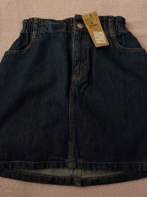 Mörkblå jeanskjol med resårmidja - Trendig mörkblå jeanskjol från KappAhl med resår i midjan, knapp och dragkedja framtill samt fickor både fram och bak. Klassisk denimlook som är enkel att matcha till olika stilar.