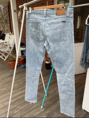 Ljusblå jeans från Nudie Jeans - Säljer ett par ljusblå jeans från Nudie Jeans med klassisk femficksmodell och raka ben. Jeansen har en snygg tvättad look och är tillverkade i bomull. Perfekta för dig som gillar en avslappnad och stilren stil.