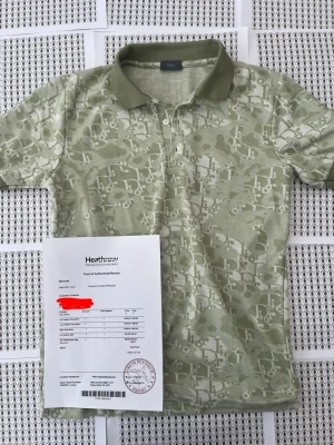 Grön mönstrad polo från D - Säljer en grön kortärmad pikétröja från D med diskret mönster i ljusare toner och klassisk krage. Tröjan har knappslå framtill och är tillverkad i mjukt bomullsmaterial. Perfekt för dig som vill ha en exklusiv och unik look.