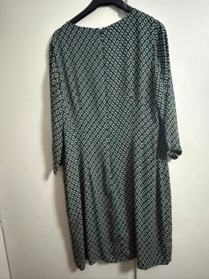 Grönvit mönstrad klänning från  STOCKH LM - Mönstrad klänning från Stockh LM i grönt och vitt med grafiskt rutmönster. Klänningen har rund halsringning och trekvartsärm. Lätt och luftig modell som slutar vid knäna. Perfekt för dig som gillar en avslappnad men snygg stil.