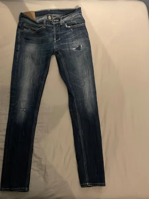Mörkblå Dondup jeans slim  - Säljer ett par mörkblå Dondup jeans med snygga slitningar och tvättade detaljer i modellen George. Jeansen har fem fickor, låg midja och kontrastsömmar. Perfekta för en avslappnad och trendig look.
