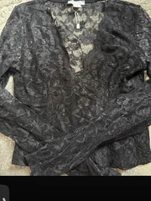 Svart spetsblus från Amisu - Säljer en svart långärmad spetsblus från Amisu. Blusen har ett genombrutet blommigt spetsmönster och djup v-ringning. Perfekt för dig som vill ha en trendig och elegant topp med snygga detaljer. Tillverkad i ett tunt och stretchigt material.