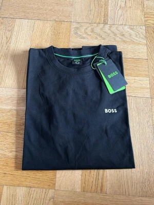 Svart BOSS t-shirt med logga - Snygg svart t-shirt från BOSS med klassisk passform och liten vit BOSS-logga på bröstet. T-shirten har rund halsringning, korta ärmar och är tillverkad i mjuk bomull. Perfekt basplagg för en clean och stilren look.