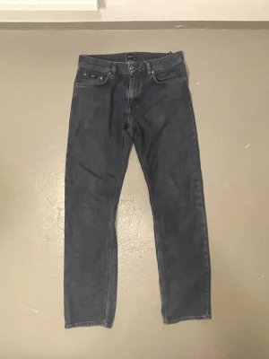 Mörkblå jeans från BOSS - Säljer ett par mörkblå jeans från BOSS med klassisk femficksdesign och raka ben. Jeansen har snygga detaljer vid fickorna och är tillverkade i slitstark denim. Perfekt för dig som vill ha ett stilrent och tidlöst plagg i garderoben.