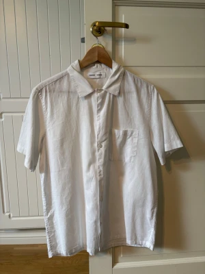 Vit linneskjorta från Samsøe Samsøe - Klassisk vit skjorta från Samsøe Samsøe i linne med korta ärmar och bröstficka. Skjortan har knappar framtill och en avslappnad passform, perfekt för varma dagar.