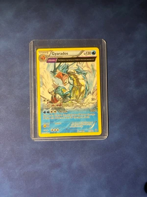 Pokémonkort Gyarados i plastficka - Säljer ett Gyarados Pokémonkort med gul ram och färgstark illustration. Kortet ligger i en genomskinlig plastficka och har blå, gul och röd design. Perfekt för samlare eller Pokémonfans som vill utöka sin kortsamling.