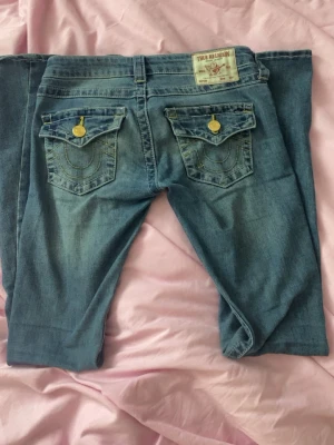 Blå bootcut jeans från True Religion - Säljer ett par blå bootcut jeans från True Religion med ikoniska fickor bak och guldknappar. Säljer då dom inte kommer till användning längre, finns lite skador längst ner vid fötterna (se bild 4) men inget som syns, passar mig perfekt som oftas bär storlek xs och är 167, hör av er vid frågor 