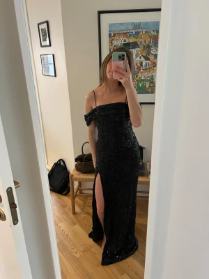 Svart paljettklänning med slits - Helt ny och oanvänd från showpo! Säljer en lång svart klänning täckt av paljetter med smala axelband och off shoulder-detalj. Klänningen har en slits framtill och figurnära passform.