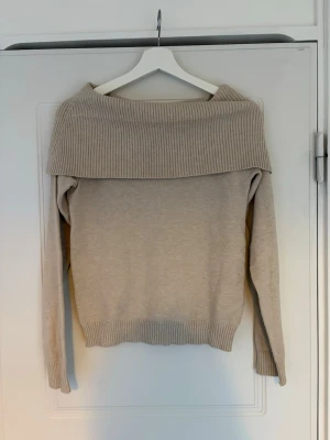 Beige off shoulder stickad tröja Lindex - Beige stickad tröja från Lindex med bred ribbad off shoulder-krage. Långärmad modell med ribbade muddar vid ärmslut och nederkant. Perfekt för en chill och stilren look.