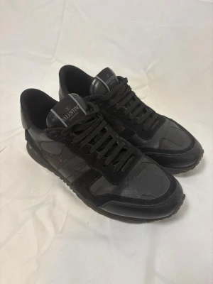 Valentino Rockrunners - Snygga helsvarta sneakers från Valentino med klassisk låg siluett. Skorna har en mix av läder och mocka i ovandelen, svarta skosnören och diskret logga på plösen. Perfekta för dig som gillar stilrena och exklusiva sneakers. 40 passar 41