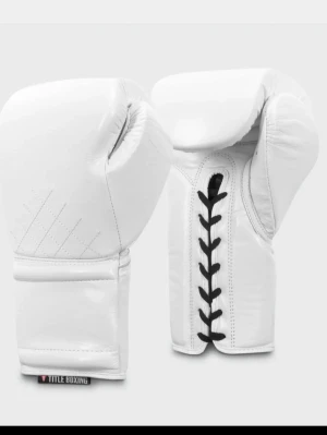 Vita boxningshandskar Title Boxing - Säljer ett par vita boxningshandskar från Title Boxing 16oz med klassisk snörning i svart. Handskarna är tillverkade i slitstarkt konstläder och har en stilren, clean look. Perfekta för träning eller sparring. Använt ca 3-4 gånger ser helt nya ut. Nypris är 1299kr, Priset kan diskuteras vid snabb affär.