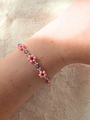 Handgjort rosa armband med blommor 🌸 - Handgjort armband med små rosa blommor och lila detaljer 🌸 Ett sött och feminint smycke som passar perfekt till en mjuk och romantisk stil.  Lätt att bära och fint både ensam eller tillsammans med andra armband.  ✨ Detaljer: 	• Ca 17 cm•	Handgjort 	•	Rosa blomdesign med lila inslag 	•	Silverfärgade pärlor 	•	Lätt och bekvämt  Passar till: sommar, vardag, presenter, coquette / soft girl stil 
