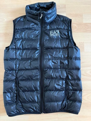 Emporio Armani Väst – Svart – 14A / 160 cm - Säljer en svart Emporio Armani-väst i storlek 14A (160 cm). Knappt använd och i mycket fint skick.  ✔️ Storlek: 14A / 160 cm ✔️ Märke: Emporio Armani ✔️ Skick: Som ny ✔️ Stilren och klassisk  Skickas väl emballerad. Fråga gärna om du vill se fler bilder!