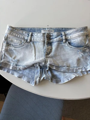 Ljusblå lågmidjade jeansshorts - Säljer ett par ljusblå lågmidjade jeansshorts från Tally weijl med slitna detaljer och dubbla knappar framtill. Shortsen har fem fickor, bälteshällor och en klassisk denimlook. Midjemåttet rakt över är 41 cm. Kolla min profil för fler snygga sommarplagg! Pris kan diskuteras 