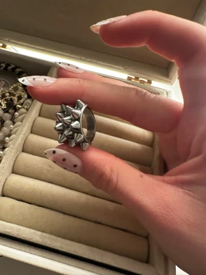 Silvrig ring med nitar - Cool ring i silverfärgad metall med flera konformade nitar på ovansidan. Ringen har en bred design och ger en edgy, alternativ vibe. Perfekt för dig som gillar statement-smycken och vill sticka ut lite extra.