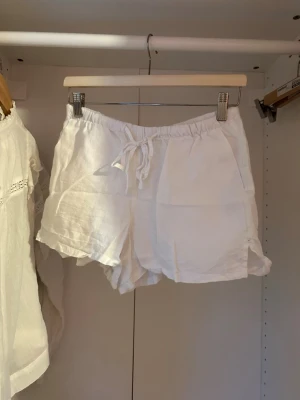 Vita linneshorts med snörning - Snygga och luftiga vita shorts i linne med elastisk midja och snörning framtill. Perfekta för varma dagar och har en avslappnad passform. Klassisk design utan mönster eller extra detaljer.