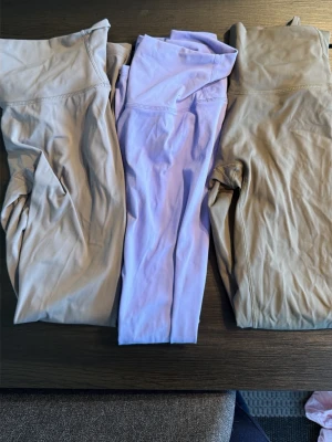 3 par tights i beige och lila - Säljer fyra par tights i mjukt och stretchigt material, ett par i  beige och ett i ljuslila och ett par militärgröna samt ett par svarta.  Perfekta för träning eller chill. Hög midja och sömlös design för skön passform. Passar dig som gillar stilrena färger och bekväma sportkläder. Små i storleken