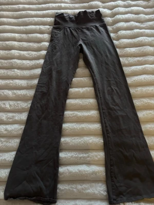 Grå bootcut yogapants från Nelly - Säljer ett par gråa yogapants från Nelly i storlek XXS. Tillverkade i mjukt och stretchigt material som sitter skönt på kroppen. Perfekta för dig som vill ha både stil och komfort. En liten blekt fläck på benet men inget man tänker på (se sista bilden). Mått: 30cm rakt över i midjan men är väldigt stretchiga och passar xs/xxs. Innerbenslängd 73cm