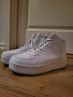 Vita high top sneakers med platåsula - Stilrena vita high top sneakers med kraftig platåsula och klassisk snörning. Skorna har perforerade detaljer på tån för extra ventilation och är tillverkade i syntetmaterial med en clean look. Perfekta för dig som vill ha en modern och sportig stil.