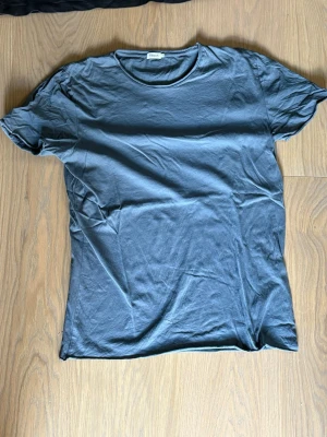 Mörkgrå t-shirt från Filippa K - En stilren mörkgrå t-shirt från Filippa K med rund halsringning och klassisk passform. Tillverkad i mjuk bomull som känns skön mot huden. Perfekt basplagg för alla tillfällen och enkel att matcha med olika outfits.