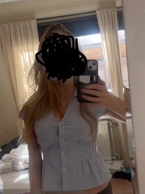 Blårandig blus med v-ringning - Snygg blårandig blus från Gina med v-ringning och knappar framtill. Blusen har korta ärmar, markerad midja med smockdetaljer och en lätt utsvängd nederdel. Tillverkad i ett tunt, skönt bomullsmaterial som passar perfekt till jeans eller kjol. Helt oanvänd, endast provad!! Slutsåld!! 