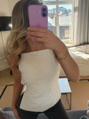 Vit  linnetopp med öppen rygg - Säljer en stilren vit linnetopp med raka linjer och tunna axelband. Toppen har en öppen rygg med smala band som ger en snygg och modern look. Perfekt att matcha med jeans eller kjol för en trendig outfit.