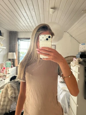 Beige kortärmad t-shirt - En enkel beige t-shirt med korta ärmar och rund hals. T-shirten har vita kanter vid ärmslut och halsringning för en stilren kontrast. Passformen är normal och materialet ser ut att vara mjuk bomull, perfekt för en avslappnad look.