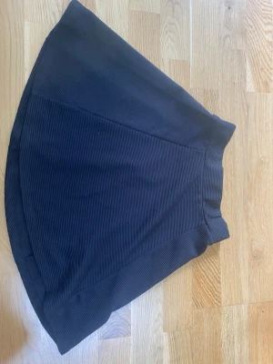 Svart kortkjol från Divided XS - Säljer en svart kortkjol från Divided i storlek XS. Kjolen har en lätt utställd form, ribbad struktur och dragkedja bak. Perfekt att matcha med en crop top eller stickad tröja för en trendig look.