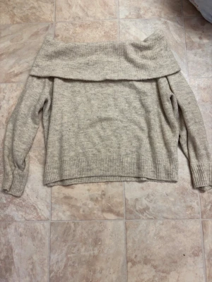 Beige off shoulder stickad tröja - Säljer en beige stickad off shoulder-tröja med bred krage och långa ärmar. Tröjan har ribbstickade muddar vid ärmslut och nederkant. Perfekt för dig som gillar en avslappnad men ändå trendig stil.