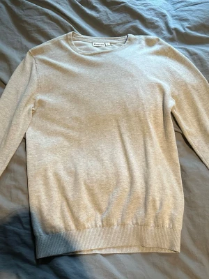Stickad tröja från Kappahl - En stilren beige tröja från Kappahl i storlek S. Tröjan har rund halsringning, långa ärmar och ribbade muddar vid ärmslut och nederkant. Perfekt basplagg i mjukt material som passar till det mesta.