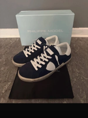Philippe Model Mörblå suede Prsx Low - Snygga sneakers från Philippe Model i marinblå mocka med vita detaljer och vita skosnören. Klassisk låg modell med vit sula och logotypdetaljer på sidan. Perfekta för dig som gillar stilrena och trendiga skor.